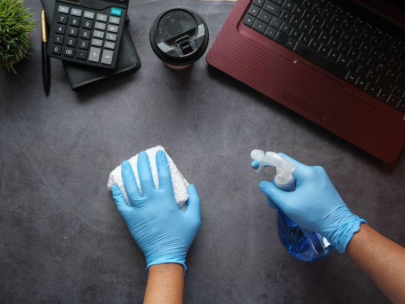 Two hands, one holding a cloth and the other wiping a desk surface, removing dust and dirt.